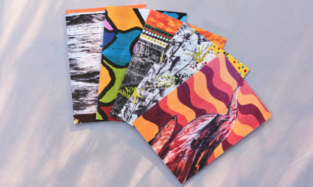 A fan of small, colourful art cards arranged in a loose stack on a light fabric surface. Each card features bold, abstract patterns and textures in warm tones.